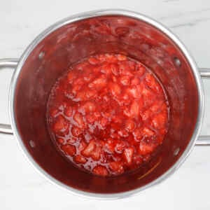 Sebuah panci berisi isian stroberi yang sudah dimasak, memperlihatkan potongan-potongan stroberi dalam saus merah mengkilap.