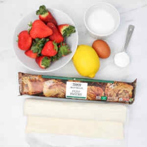 Bahan-bahan untuk kue pai stroberi meliputi stroberi segar, lemon, telur, gula, dan adonan puff pastry.