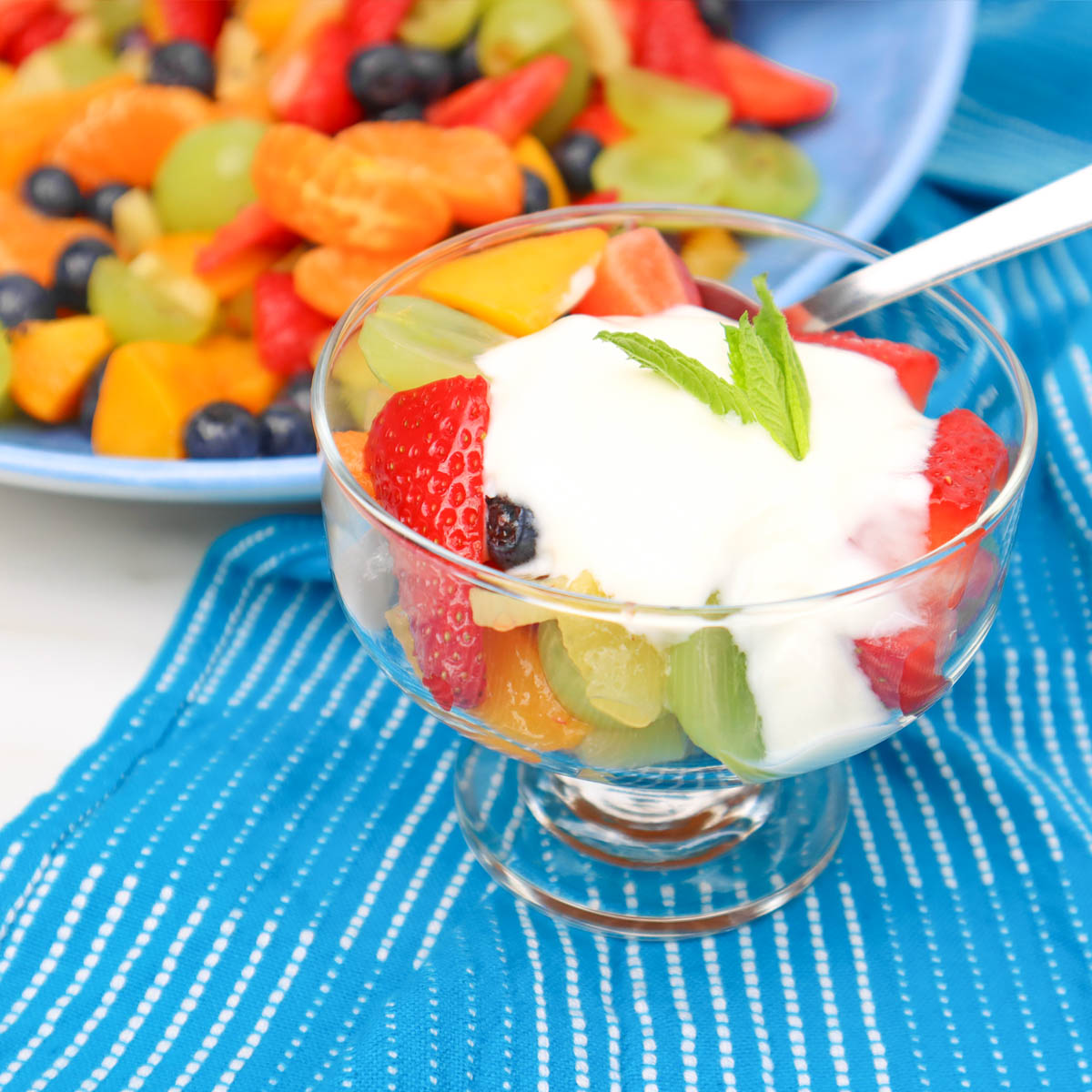 Summer Fruit Salad A glass bowl filled with colorful summer fruit salad topped with yogurt and a mint leaf.