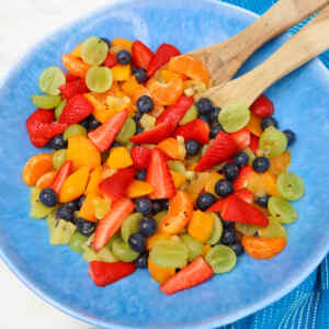 A colorful summer fruit salad with strawberries, blueberries, grapes, and mandarin oranges in a blue bowl.