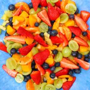A colorful summer fruit salad with strawberries, blueberries, grapes, and mandarin oranges on a blue plate.