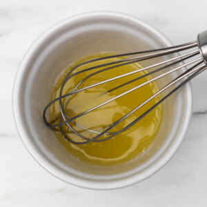 A whisk in a bowl with a yellow liquid, honey, and fresh lime or lemon juice.