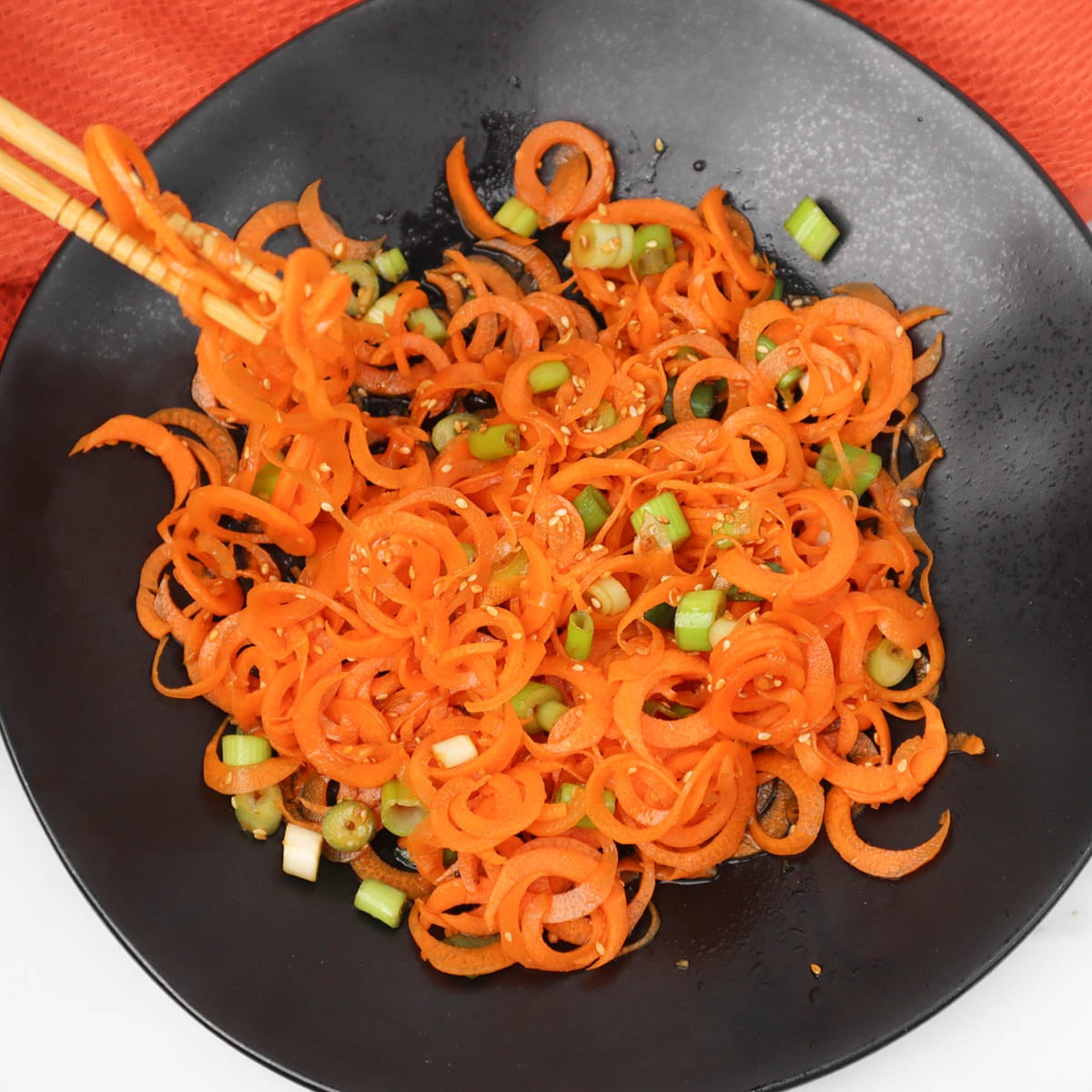 Asian carrot salad A vibrant Asian carrot salad with spiralized carrots and green onions in a black bowl.