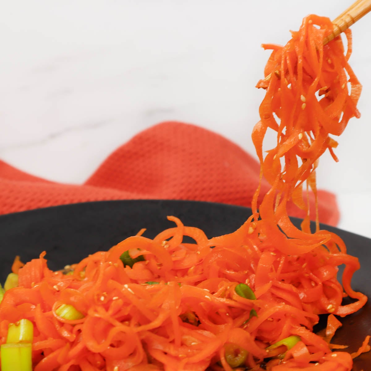 Asian carrot salad A close-up of shredded carrots in a black bowl, with chopsticks lifting some strands.