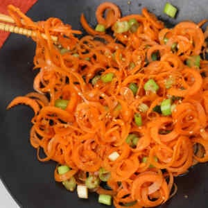 A vibrant Asian carrot salad with spiralized carrots and green onions in a black bowl.