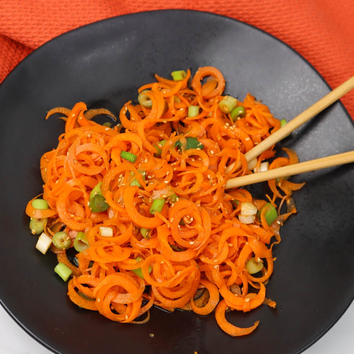 Asian carrot salad A vibrant Asian carrot salad with spiralized carrots and green onions in a black bowl.
