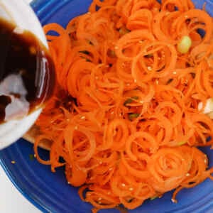 Spiralized carrots being drizzled with sauce in a blue bowl.