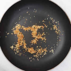 Toasted sesame seeds scattered in a black frying pan.