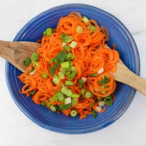 A vibrant Asian carrot salad with spiralized carrots and green onions in a blue bowl.