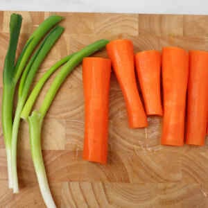 Freshly cut carrots and green onions on a wooden cutting board.