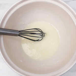 A whisk mixing a light batter in a pink bowl.