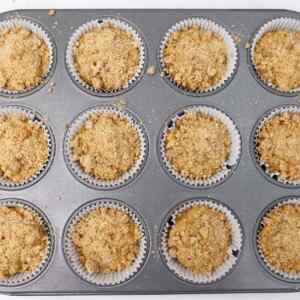 Unbaked coffee cake breakfast muffins in a muffin tin, topped with crumbly streusel.