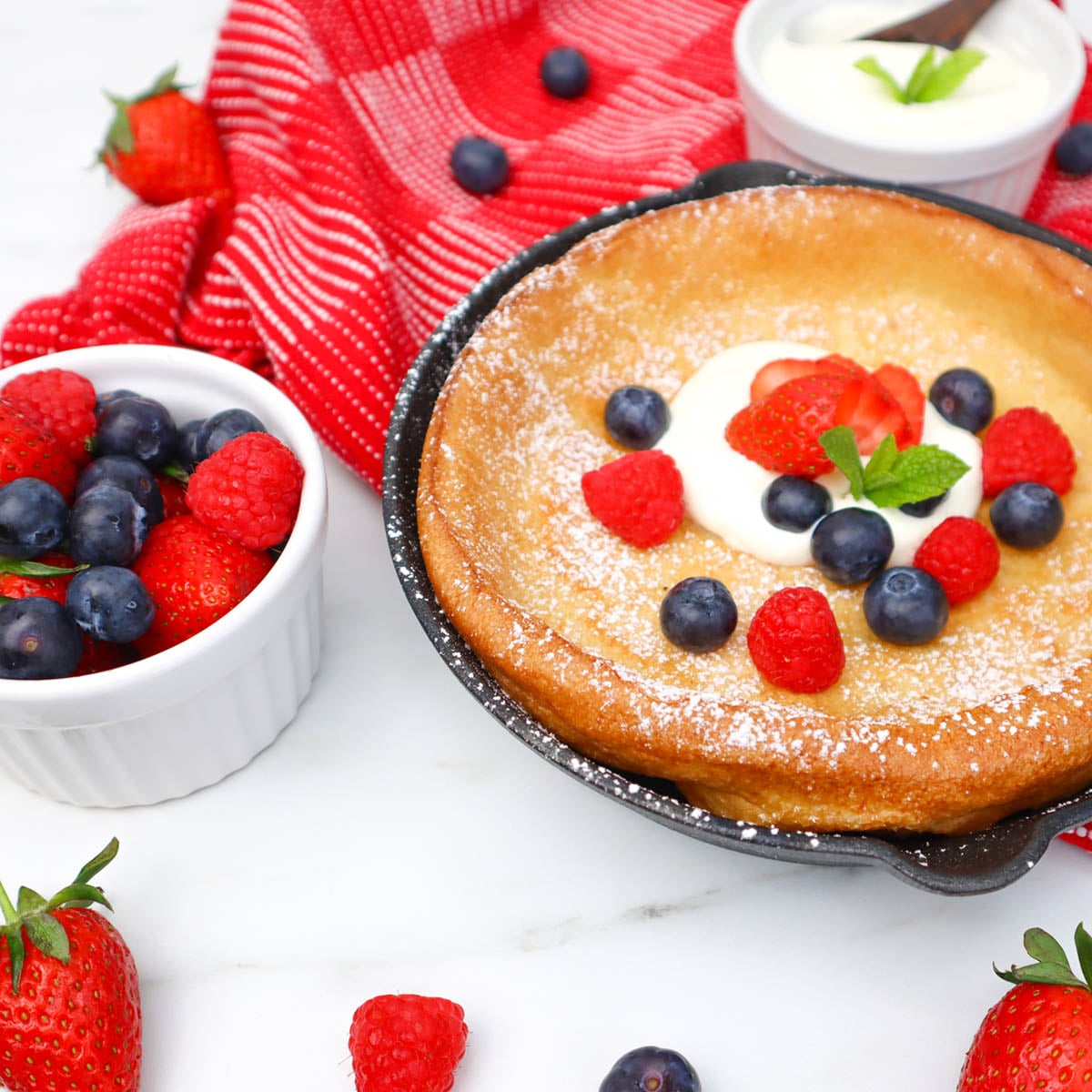 Dutch Baby Pancake Ein fluffiger Dutch Baby Pancake mit frischen Beeren und einem Klecks Sahne, serviert in einer gusseisernen Pfanne.