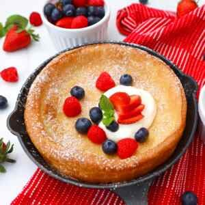 Un pequeño panqueque holandés cubierto con frutos rojos frescos y crema batida, preparado en una sartén de hierro fundido.