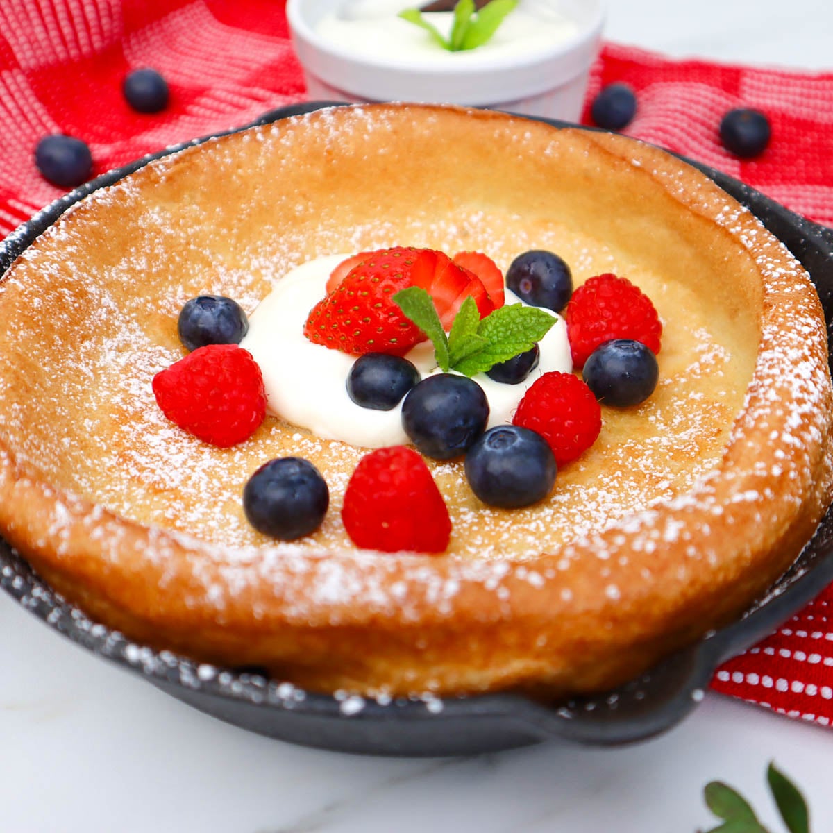 Dutch Baby Pancake Ein Dutch Baby Pfannkuchen mit Schlagsahne, Erdbeeren, Himbeeren, Blaubeeren und Minzblättern.