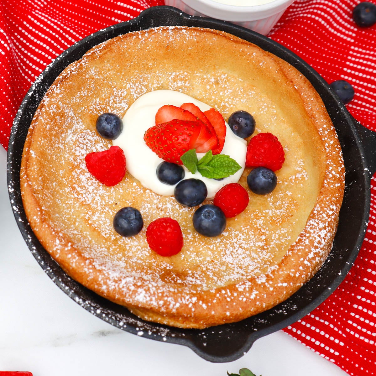 Dutch Baby Pancake Ein Dutch Baby Pfannkuchen mit Schlagsahne und frischen Beeren aus der gusseisernen Pfanne.