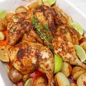 Frango assado no forno, aberto em borboleta e temperado com especiarias, servido com batatas e fatias de limão.