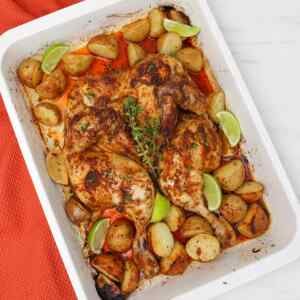 Frango assado aberto com batatas e fatias de limão em uma assadeira.