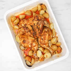 Frango assado aberto e temperado com especiarias, acompanhado de batatas douradas e fatias de limão.