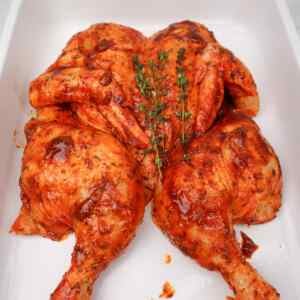 Frango aberto em borboleta, temperado com especiarias e guarnecido com tomilho fresco.