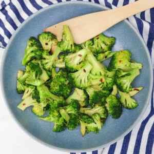 Brócoli salteado con hojuelas de chile en un plato azul con una cuchara de madera.