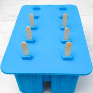 A blue popsicle mold with wooden sticks ready for making pineapple popsicles.