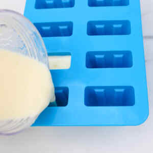 Pouring a creamy mixture into a blue popsicle mold.