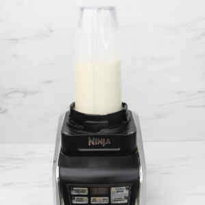 A blender filled with a creamy mixture, ready for making pineapple popsicles.
