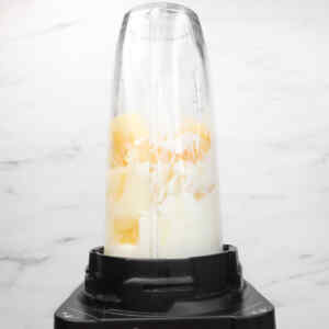 A blender filled with pineapple and cream ingredients for making popsicles.