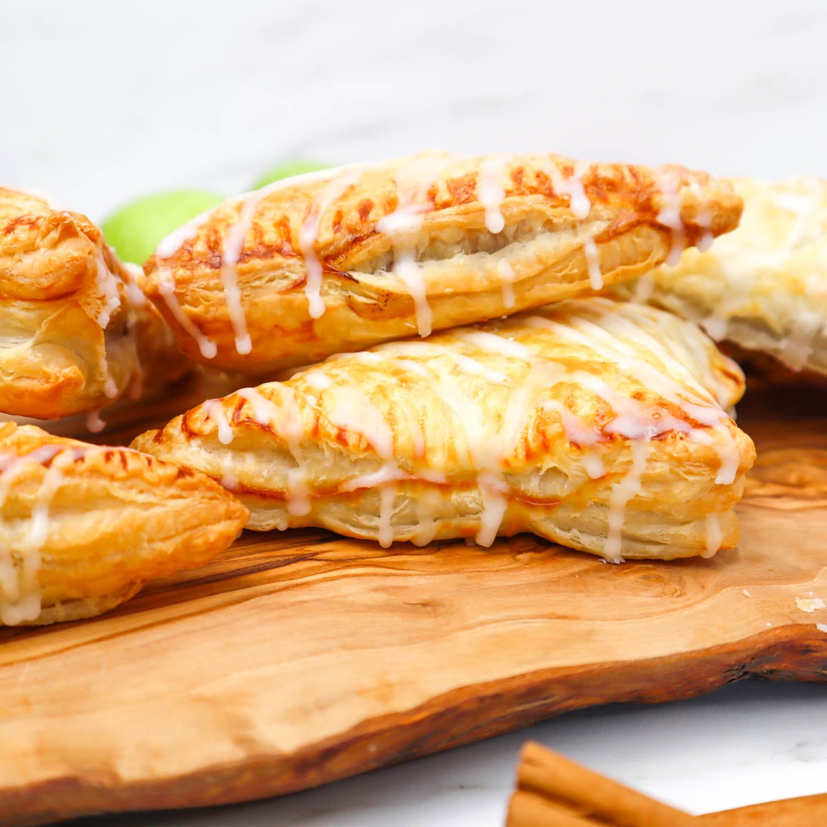 Puff Pastry Apple Turnovers Golden puff pastry apple turnovers drizzled with icing on a wooden board.