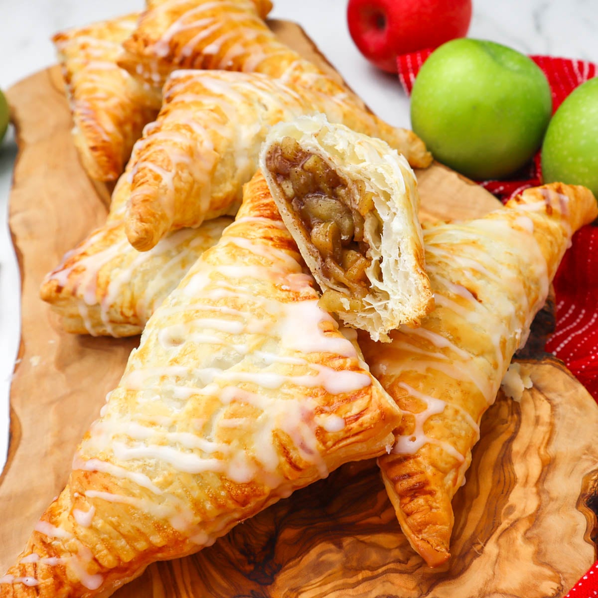 Puff Pastry Apple Turnovers Golden puff pastry apple turnovers with a drizzle of icing, showcasing a cut turnover filled with apple filling.