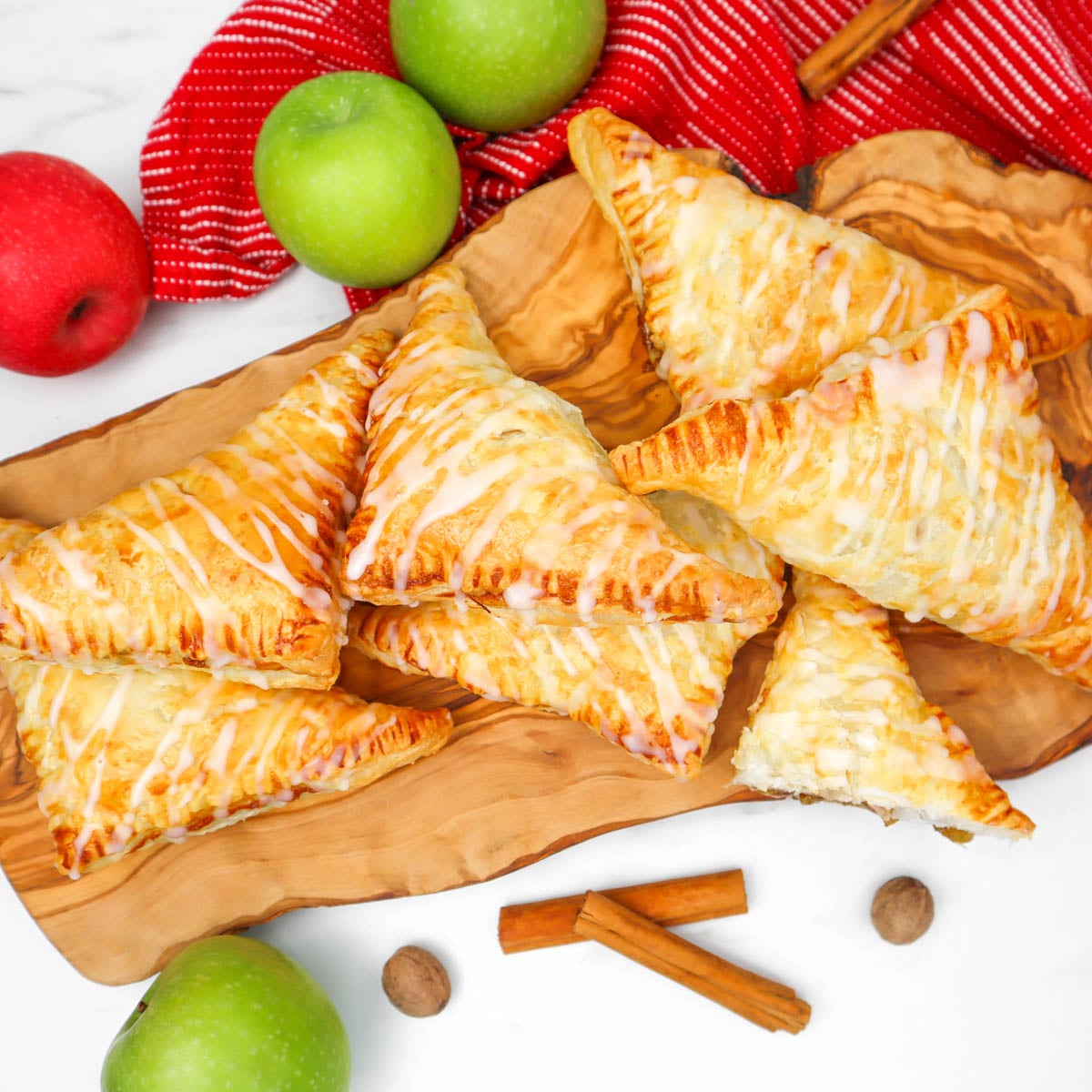 Puff Pastry Apple Turnovers Golden puff pastry apple turnovers drizzled with icing, surrounded by apples and cinnamon sticks.