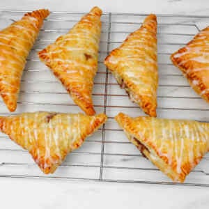 Golden puff pastry apple turnovers drizzled with icing on a cooling rack.