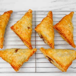 Golden brown puff pastry apple turnovers cooling on a wire rack.