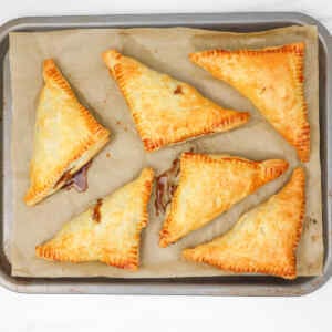 Golden puff pastry apple turnovers arranged on a baking tray lined with parchment paper.