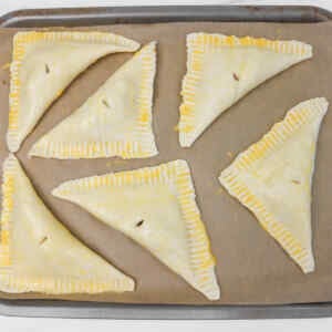 Six puff pastry apple turnovers arranged on a baking sheet lined with parchment paper.