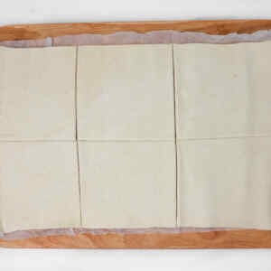 Sheet of puff pastry cut into squares on a wooden surface.