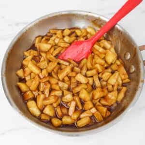 Cooked apple pieces in a pan with a red spatula, ready for turnovers.