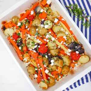 Eine Platte mit geröstetem Gemüse, darunter Karotten, Kartoffeln und Kirschtomaten, garniert mit Kräutern und Feta-Käse.