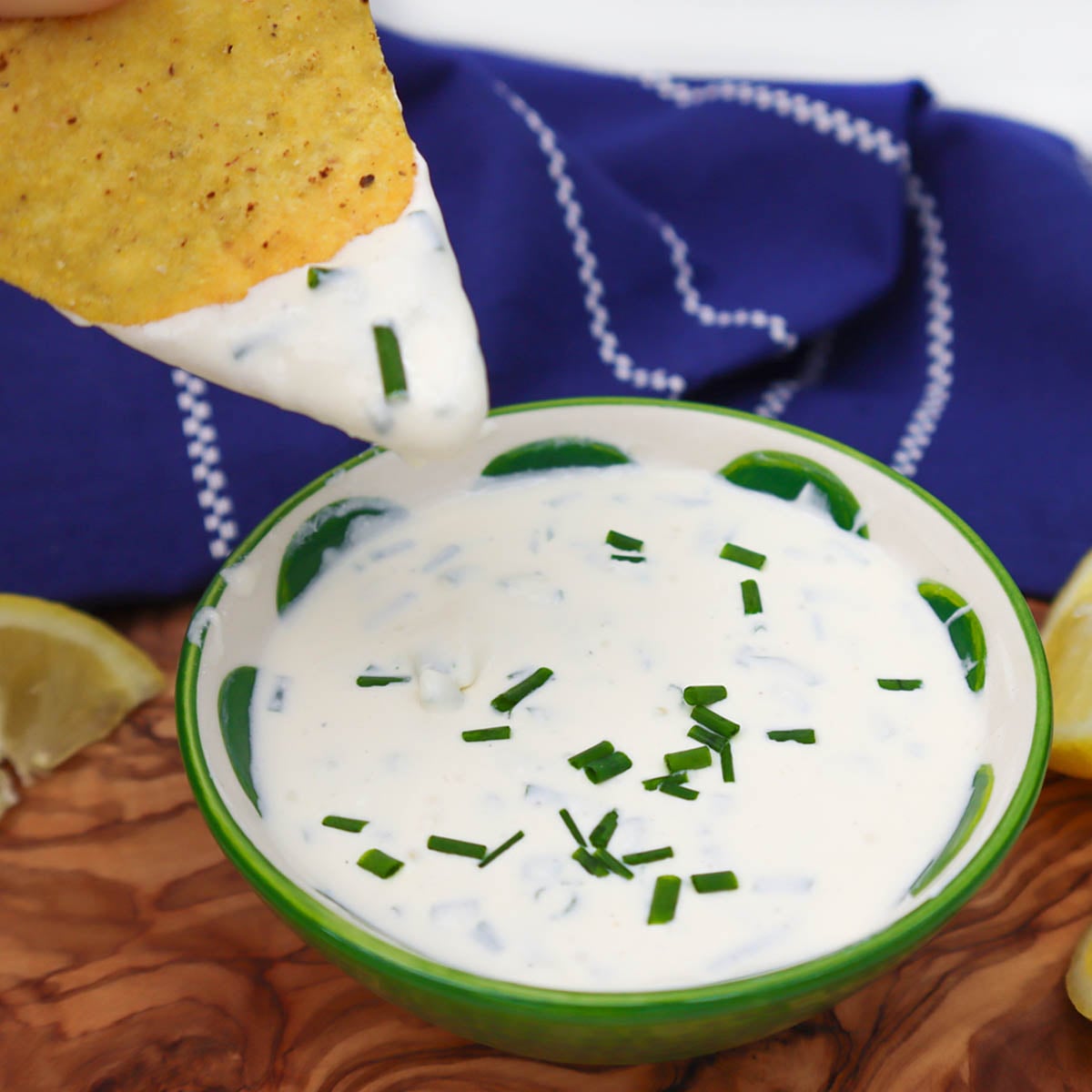 Sour Cream and Chive Dip A tortilla chip being dipped into a bowl of sour cream and chive dip garnished with fresh chives.