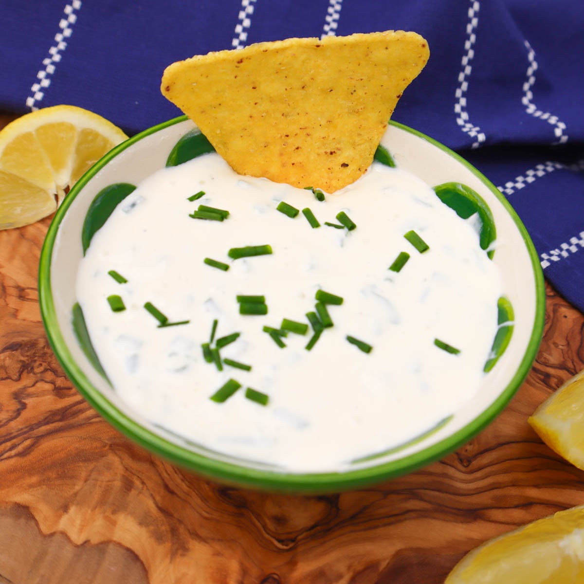 Sour Cream and Chive Dip A bowl of sour cream and chive dip garnished with chives and a tortilla chip, with lemon slices nearby.