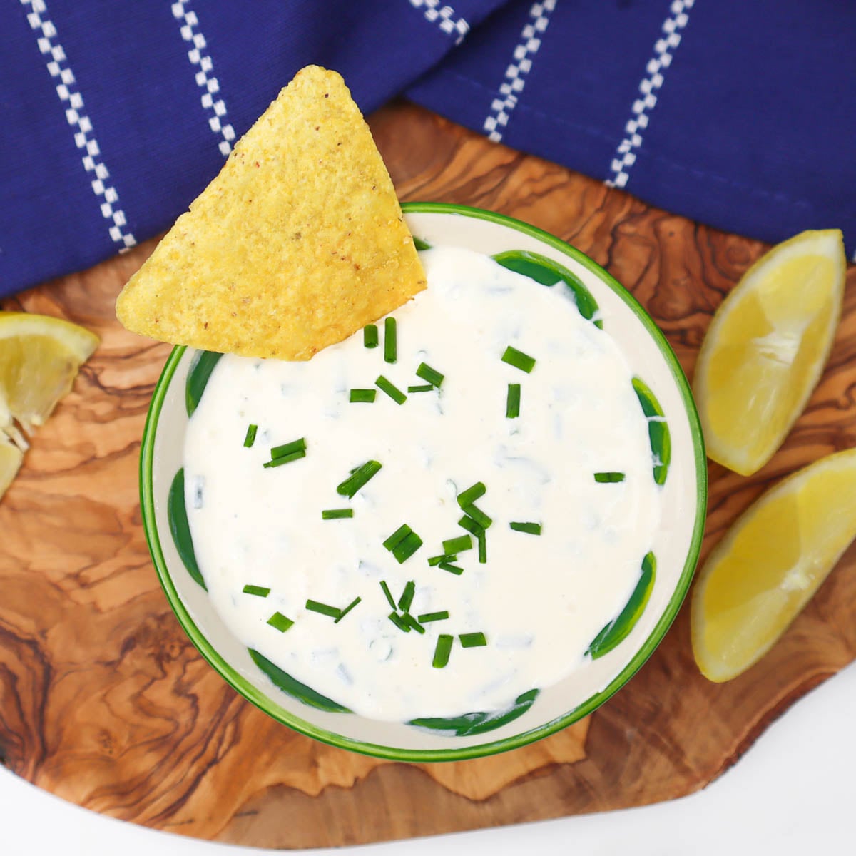 Sour Cream and Chive Dip A bowl of sour cream and chive dip garnished with chives, accompanied by a tortilla chip and lemon wedges.