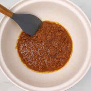 Uma tigela com uma mistura espessa, de cor caramelo, e uma espátula dentro dela.