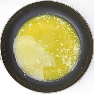 Manteiga derretida e chocolate branco em uma frigideira, prontos para o preparo dos biscoitos.