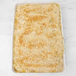A freshly baked apple crumble with a golden, crumbly topping in a white dish.