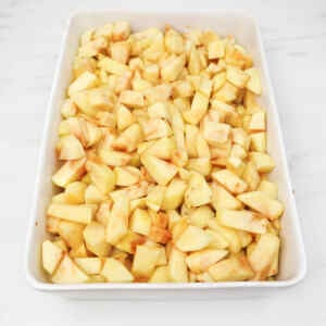 Chopped apples in a white baking dish, ready for apple crumble.