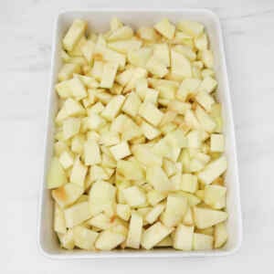 Chopped apples arranged in a white baking dish, ready for apple crumble.