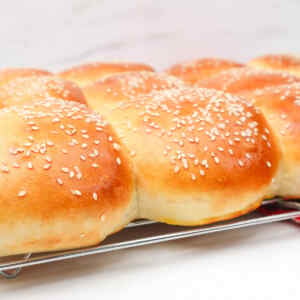 Freshly baked burger buns topped with sesame seeds on a cooling rack.