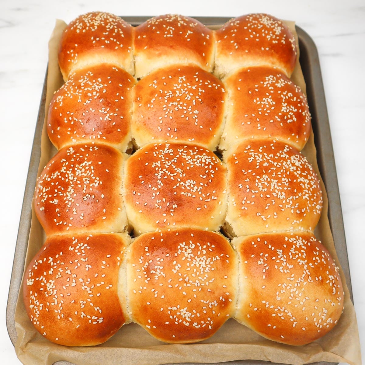 Burger Buns Freshly baked burger buns topped with sesame seeds on a baking tray.
