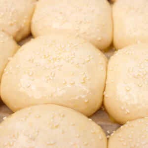 Close-up of soft, sesame-topped burger buns ready for baking.